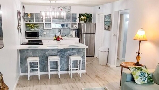 A modern kitchen with a marble island, white bar stools, and a refrigerator. - Cozy 1BR Condo - Pool & Wi-Fi (Osage Beach)