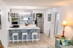A modern kitchen with a marble island, white bar stools, and a refrigerator.