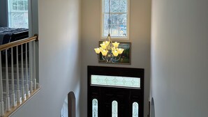 A hallway with a staircase, a chandelier, and a door with stained glass.