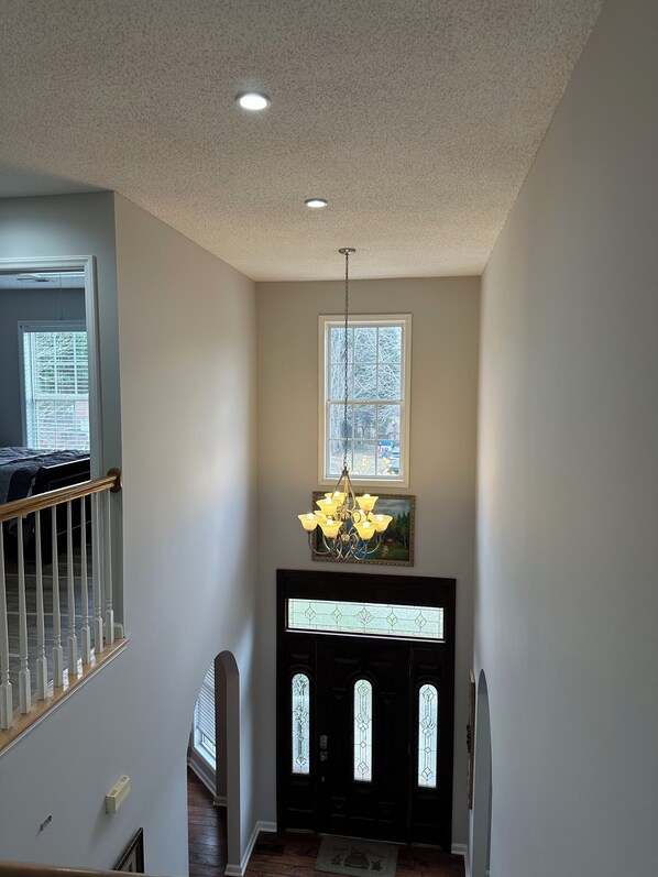 A hallway with a staircase, a chandelier, and a door with stained glass.