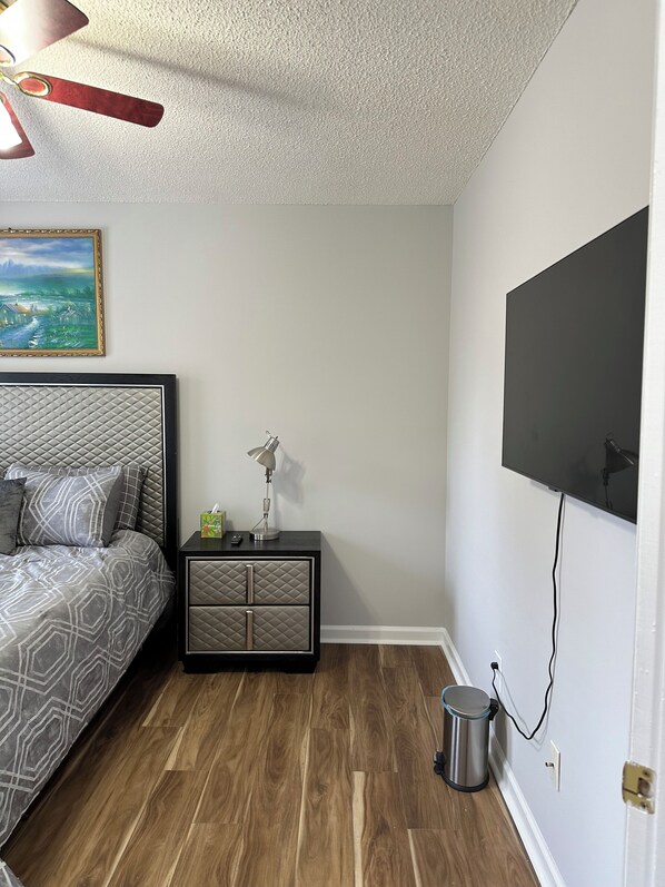 Un dormitorio con cama, mesita de noche, lámpara, televisión y un cuadro en la pared.