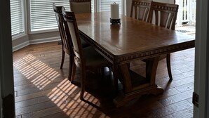 A dining room with a wooden table and chairs, a chandelier, and a sign above the windows that reads "trust me you can dance."