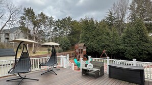 A wooden deck with outdoor furniture, including chairs and a table, and a play structure in the background.