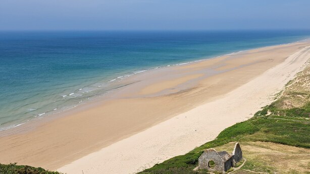 A coastal beach with a clear view of the ocean and a grassy area with a stone structure.