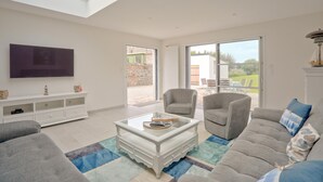 A spacious living room with a flat-screen TV, a white coffee table, and a grey sofa.