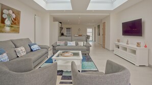 A modern living room with two grey sofas, a coffee table, and a TV on a white stand. There are skylights above the ceiling.