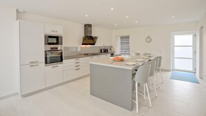 A modern kitchen with white cabinetry, a central island with bar stools, and a dining area with a large table.
