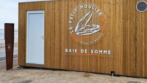 Un edificio de madera con una puerta blanca y un logotipo que dice "LE PETIT MOULIER 1983 BOUCHOT BAIE DE SOMME".