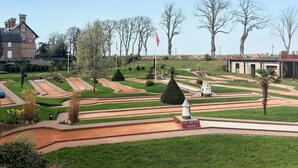 Un jardín ajardinado con senderos, una fuente y un edificio al fondo.