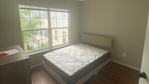 Ein Schlafzimmer mit einem Einzelbett, einem Fenster mit Jalousien, Holzboden und einem Deckenlüfter.