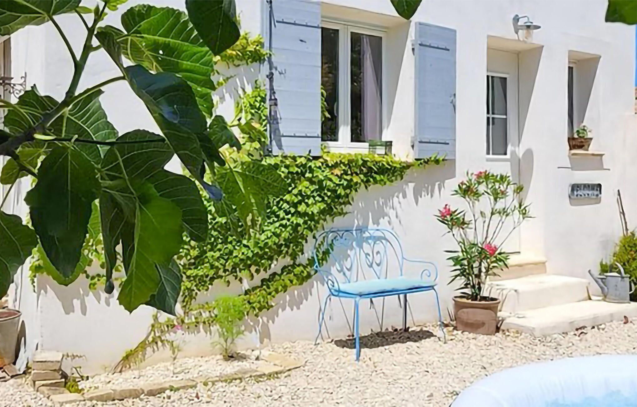 A white building with blue shutters, a blue metal bench, and potted plants.