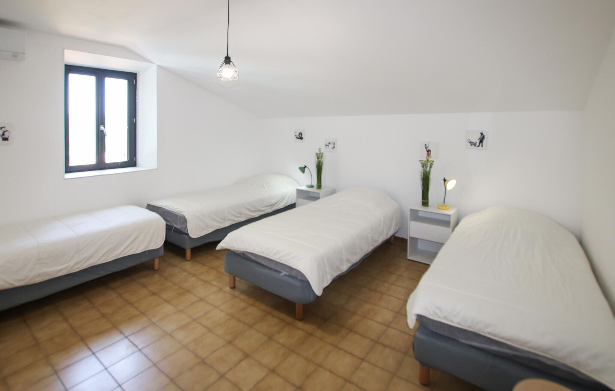 A room with three single beds, a window, and a hanging light fixture.