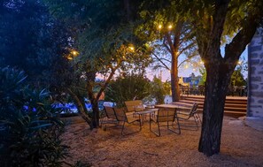 Un'area salotto all'aperto con tavoli e sedie, circondata da alberi e vista su un edificio sullo sfondo.