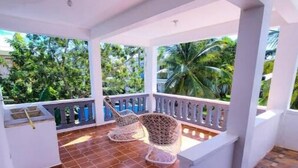 Un balcone coperto con pavimento piastrellato, ringhiere bianche e sedie in vimini.
