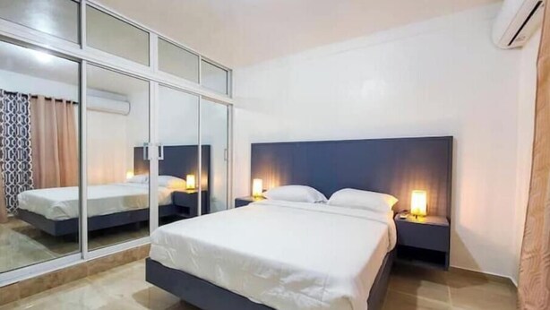 Een moderne hotelkamer met een groot bed, nachtkastjes met lampen, een glazen scheidingswand en een airconditioning.