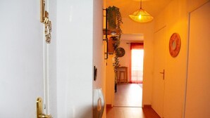 Un pasillo con una puerta blanca, una lámpara colgante, una planta en la pared y un adorno circular.