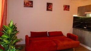 Una sala de estar con un sofá rojo, una planta en maceta y tres cuadros en la pared.