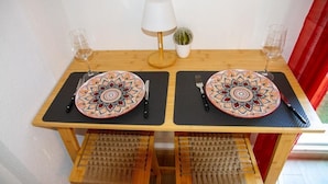 Una mesa de comedor con dos platos, cubiertos, vasos, una lámpara y una pequeña planta en maceta.