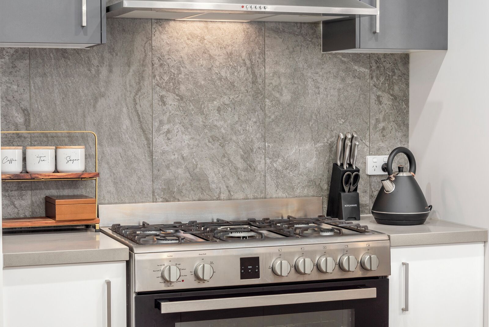 Een moderne keuken met een gasfornuis, roestvrijstalen kasten en een marmeren spatwand.