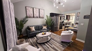 Un salon moderne avec un canapé, un fauteuil, une table basse et une vue sur la cuisine.