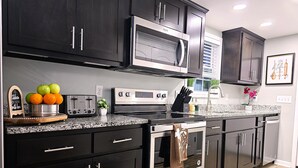 Une cuisine moderne avec des meubles de couleur sombre, des appareils électroménagers en acier inoxydable et un plan de travail en granit.