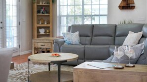 A living room with a grey sofa, a round coffee table, and a wooden side table. There are two wine glasses on the side table. - 4/3 Condo Block From Beach With Golf Cart, Hot Tub, Kayaks, Games (Indian Rocks Beach)