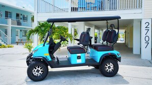 Un véhicule de golf est garé devant un immeuble doté d’un balcon et portant le numéro 2707.