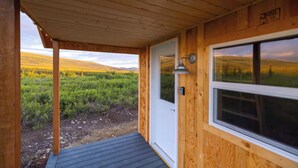 Eine Holzhütte mit Veranda, einer Tür und einem Fenster mit Blick auf ein Feld.