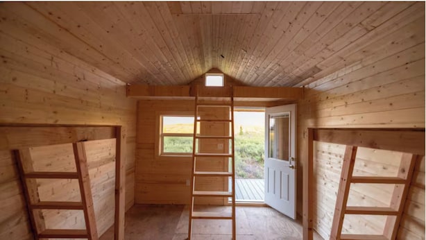 Eine Holzhütte mit Schlafzimmer auf dem Dachboden, einer Leiter zum Dachboden und einer Tür nach draußen.