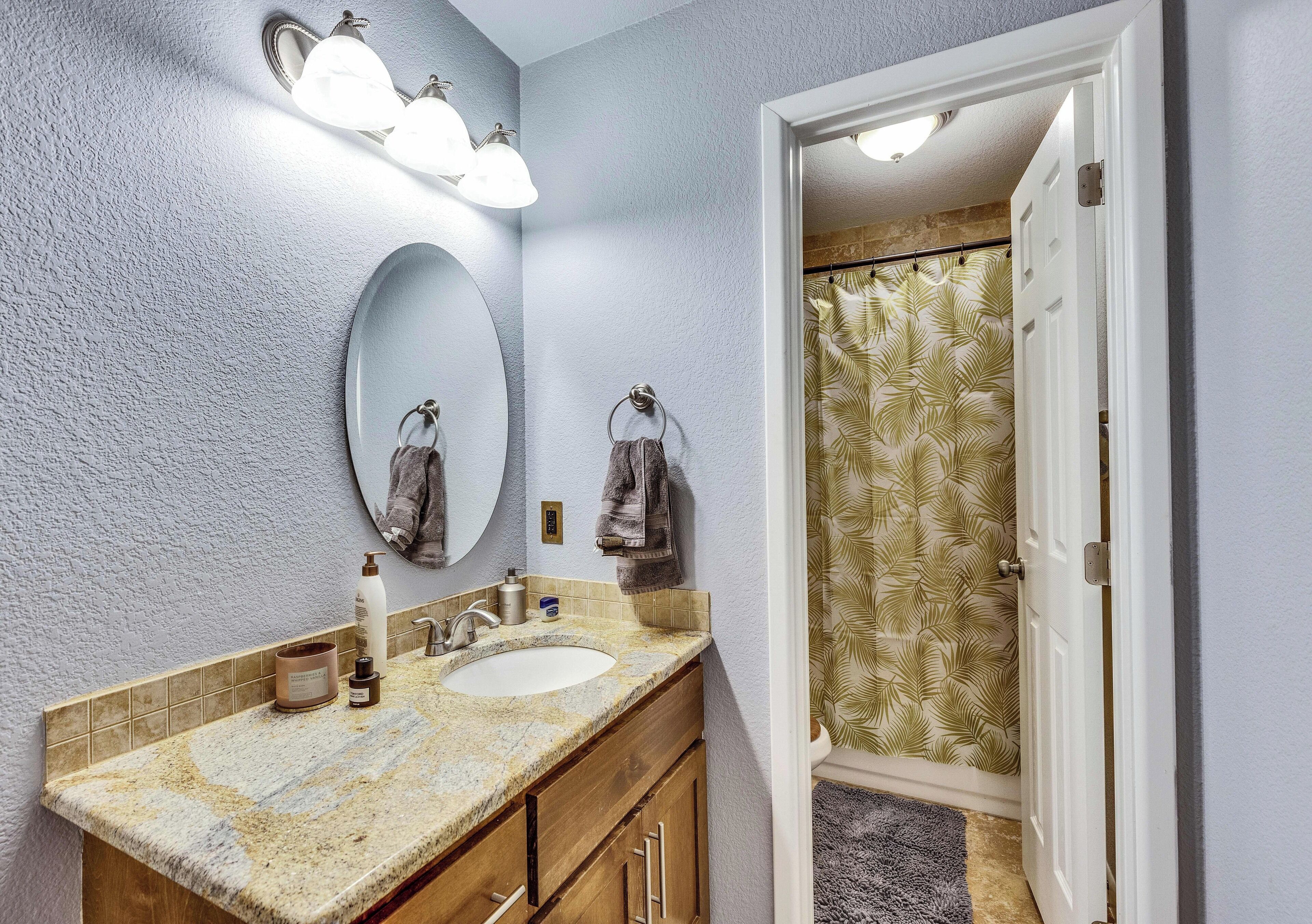 A bathroom with a granite countertop, a round mirror, and a shower with a leaf-patterned curtain.