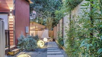 Un sendero que conduce a un edificio con terraza de madera y un pequeño jardín con un objeto esférico grande.