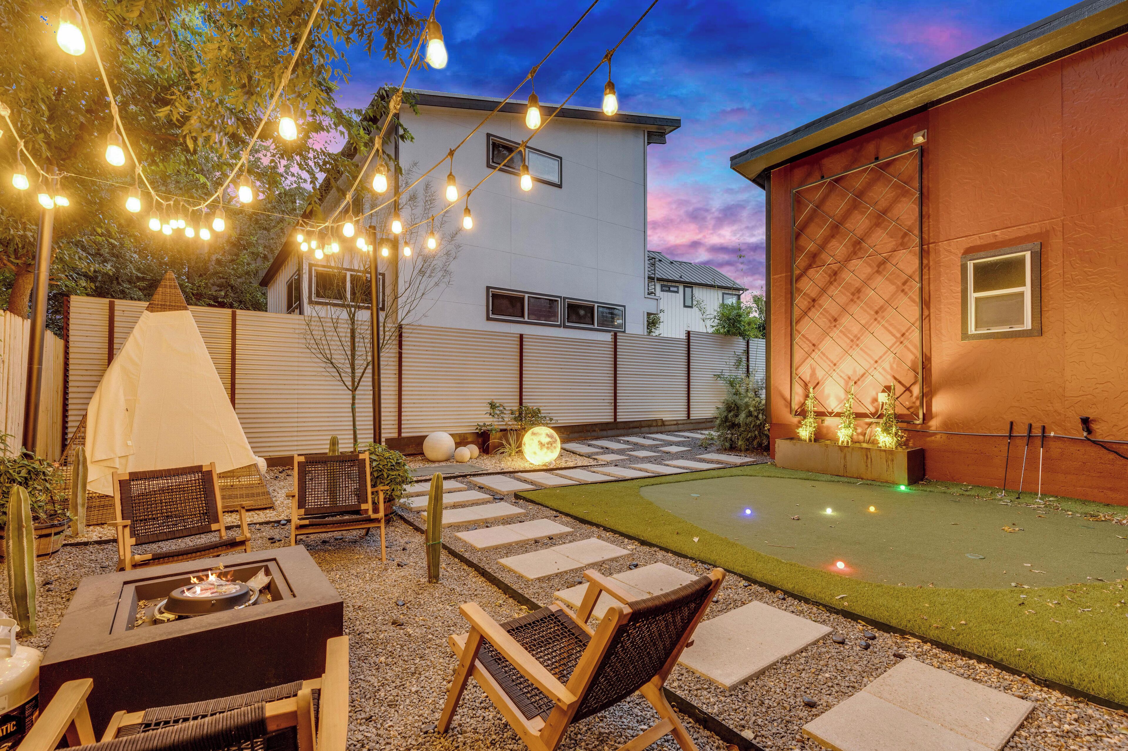 Patio trasero con fogata, mobiliario exterior, una carpa y un césped pequeño.
