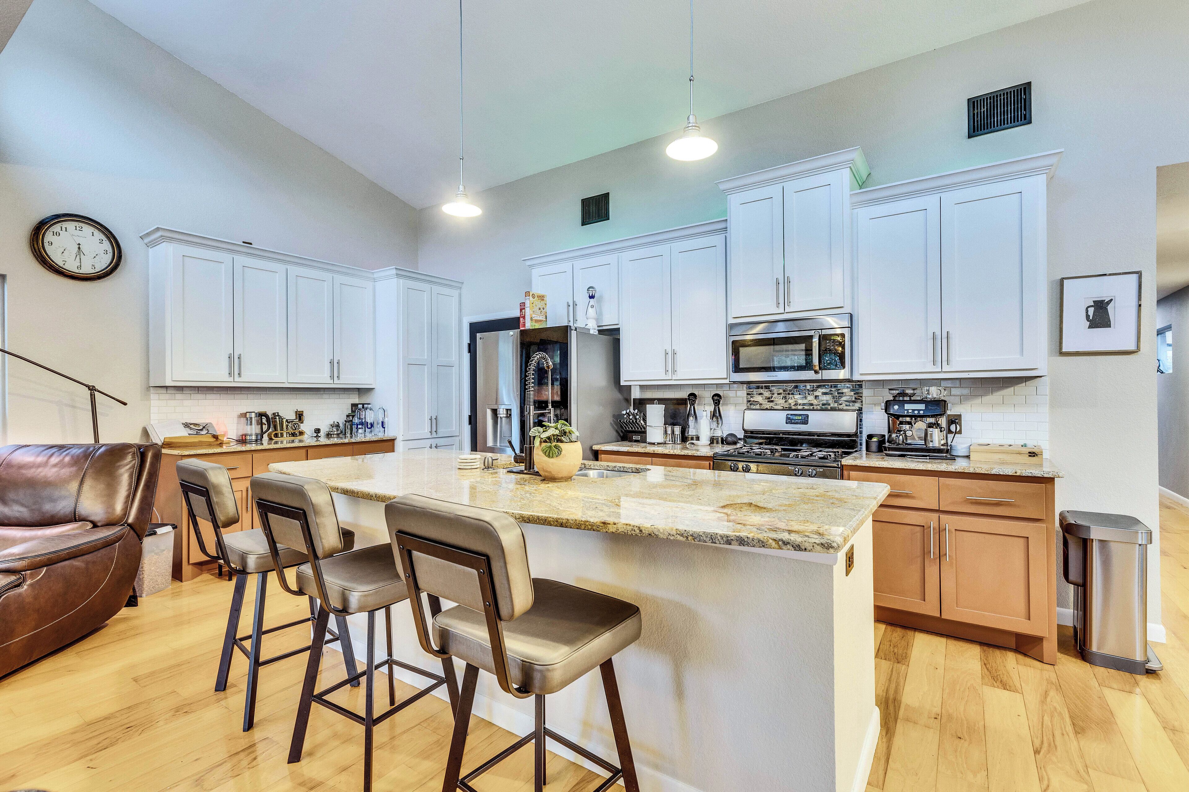 Una cocina moderna con gabinetes blancos, una isla central con taburetes y un refrigerador de acero inoxidable, además de un microondas.