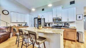 A modern kitchen with white cabinets, a central island with bar stools, a stainless steel refrigerator, and a microwave. - Walkable East Austin Oasis with Jacuzzi (Austin)