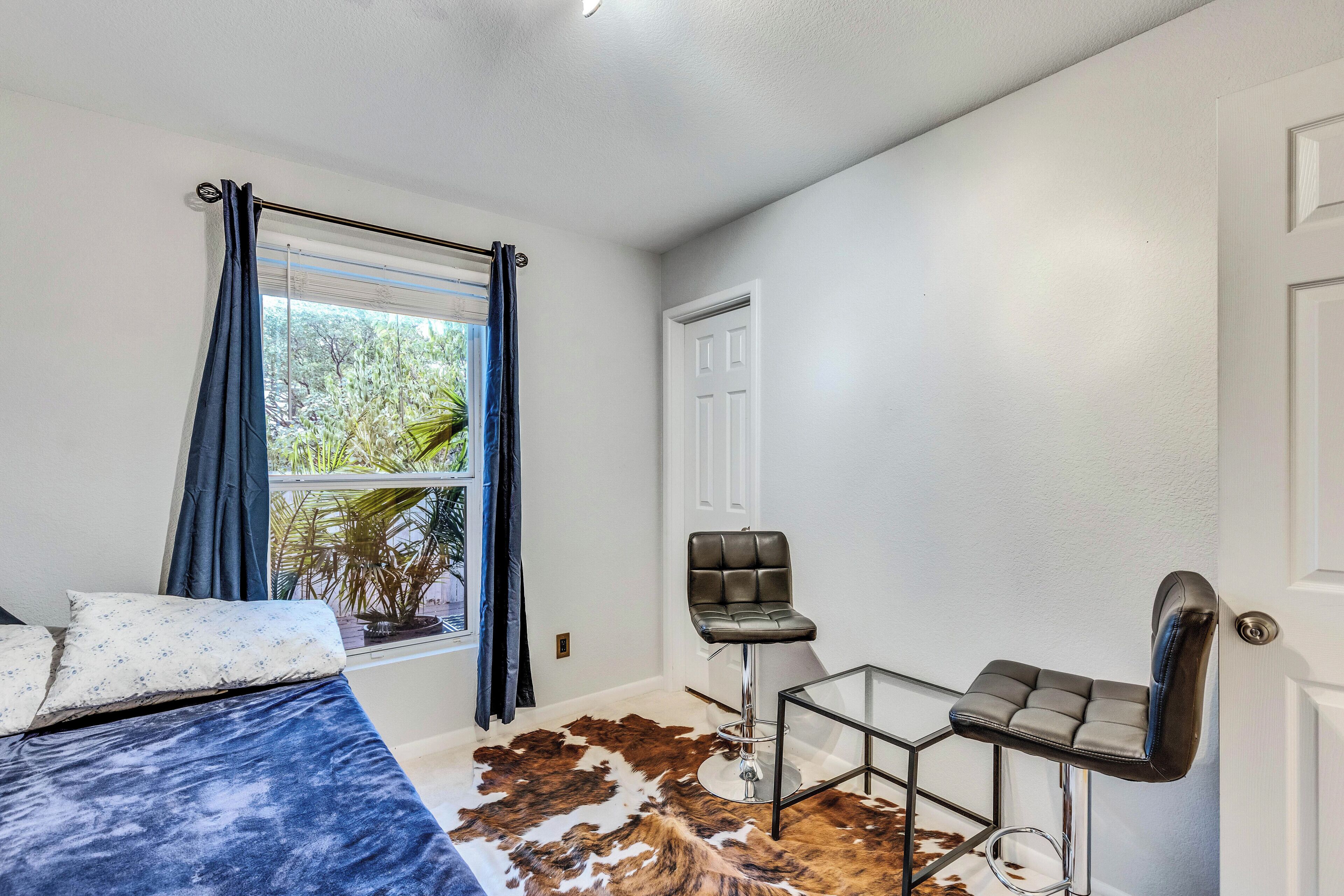 A room with a bed, a chair, a glass table, and a cowhide rug.