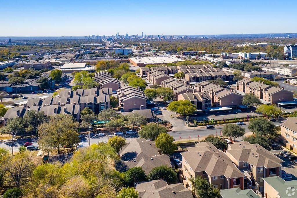 Un quartier résidentiel avec des immeubles à plusieurs étages, un parking et une vue lointaine sur les gratte-ciel de la ville.