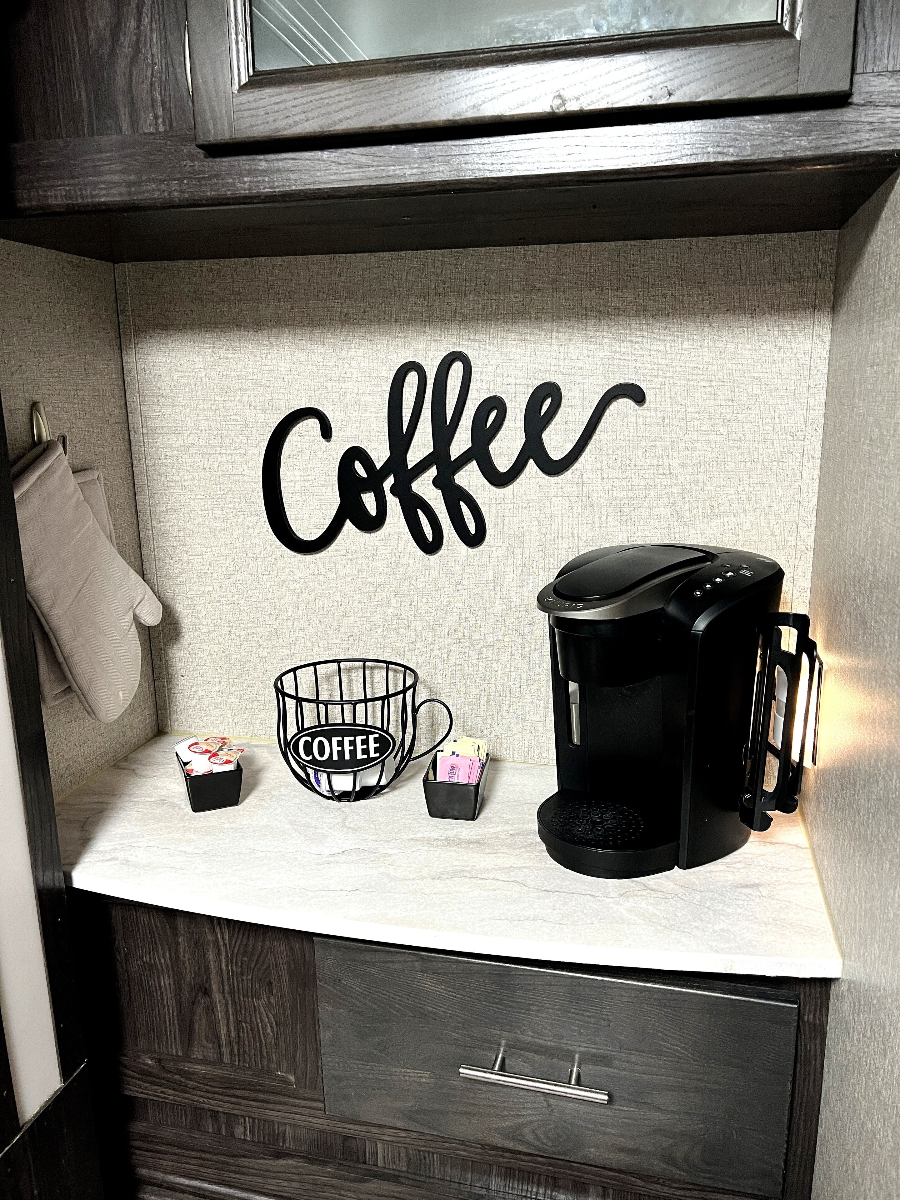 Una encimera de cocina con una cafetera, una taza de café y un cartel con motivos de café.