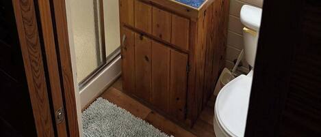A bathroom with a wooden vanity, a white sink, and a toilet. There is a glass shower door and a mirror above the sink.