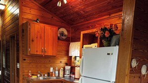 A wooden cabin kitchen with a refrigerator, wooden cabinets, a sink, and a clock on the wall.
