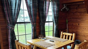 A wooden interior with a table and chairs, plaid curtains, and a view of the outdoors.