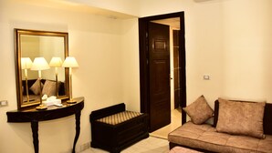 A hotel room with a console table, a mirror, a sofa, and a door leading to another room.