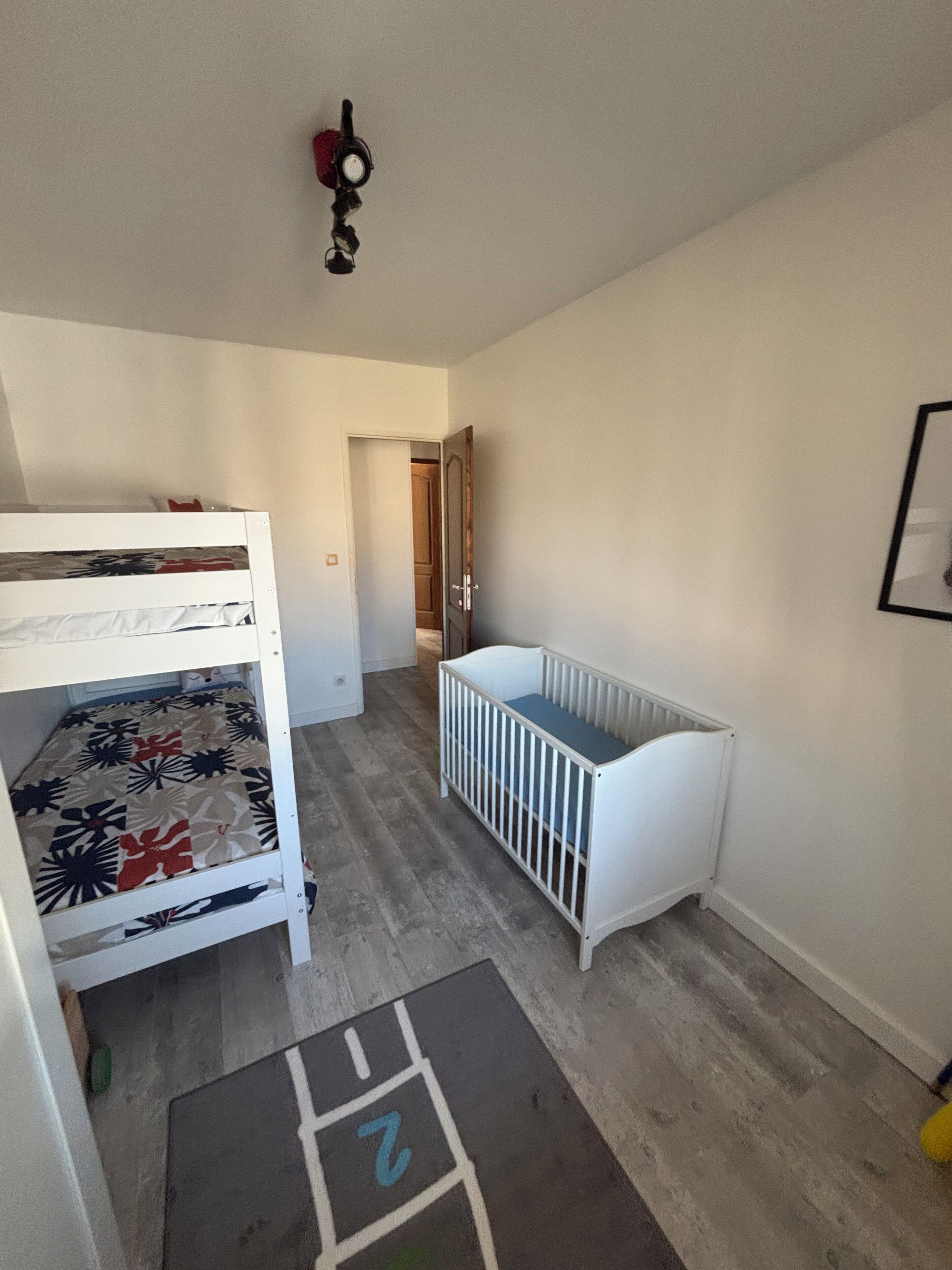 Una stanza con un letto a castello, una culla e un ingresso che conduce ad un'altra stanza.