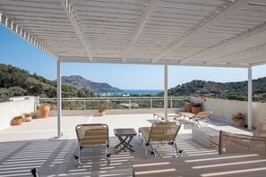 A covered outdoor seating area with a view of the sea and hills. - Antonis Apts & Retreats (Agios Vasileios)