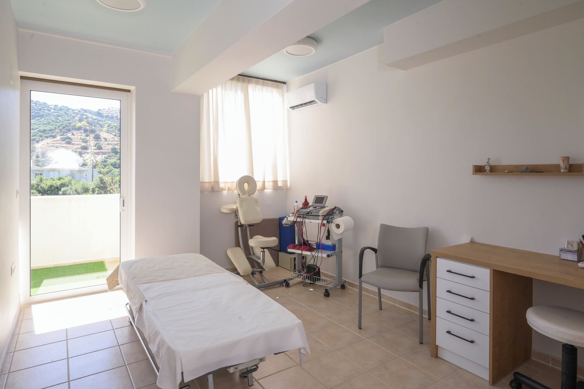 Un consultorio clínico con una cama, un escritorio, una silla y equipo médico.