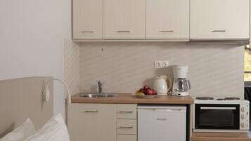 A compact hotel room with a kitchenette, a bed with pillows, and a view of the outdoors.