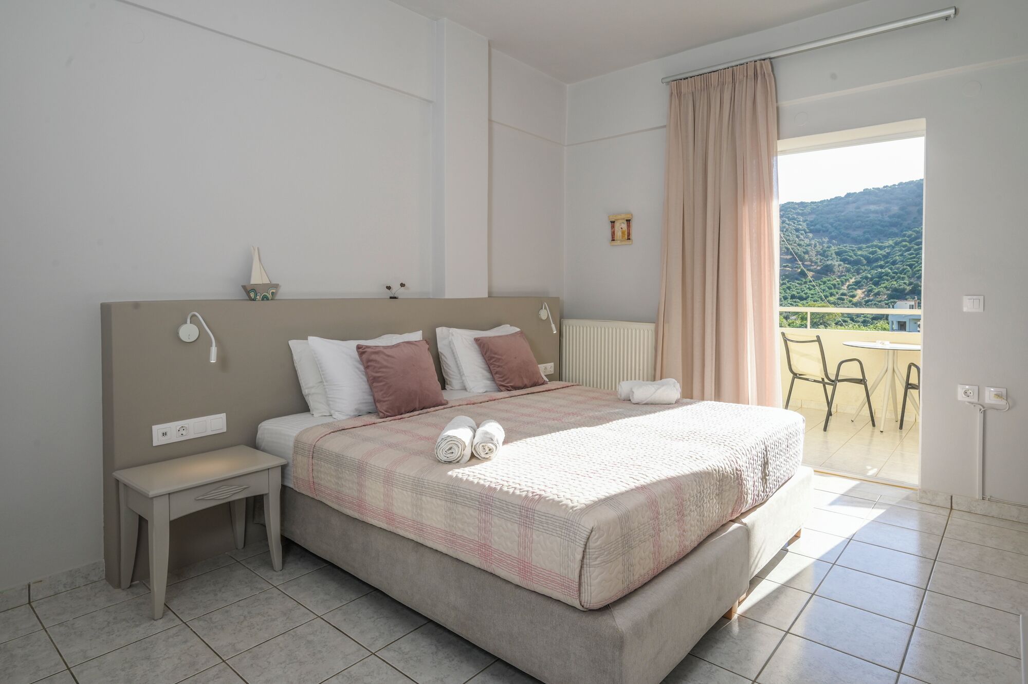 Een slaapkamer met een bed, nachtkastje en uitzicht op een balkon.