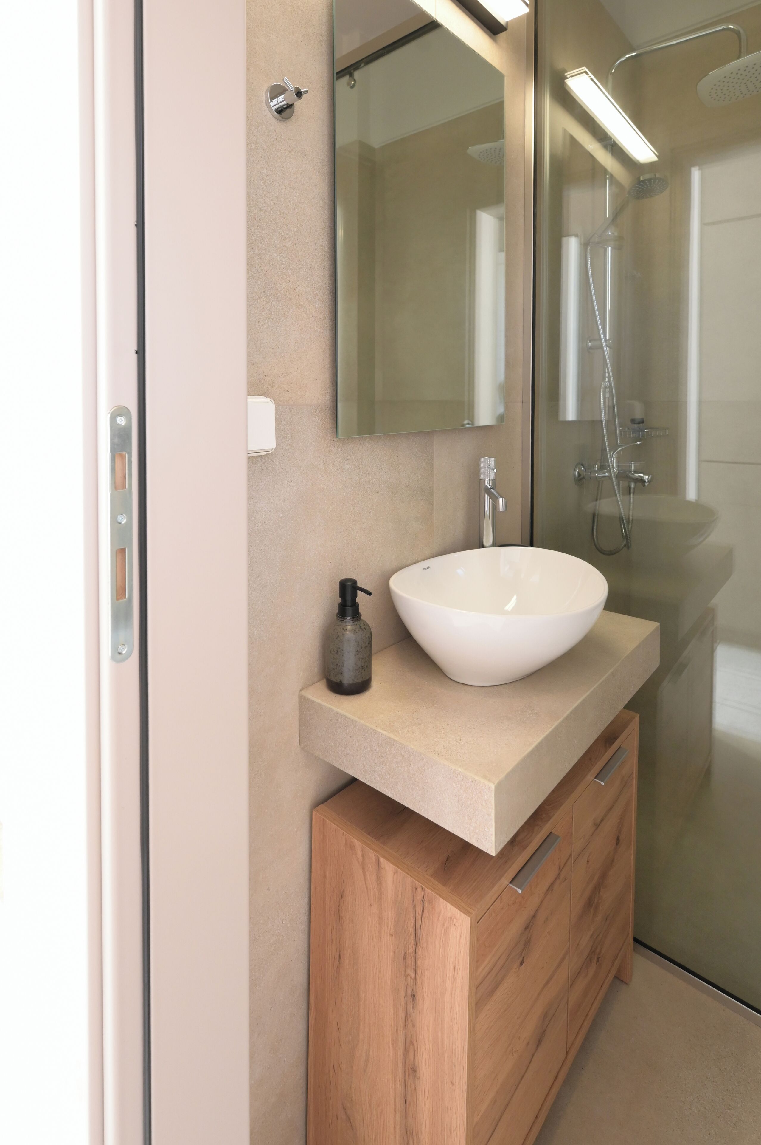 A modern bathroom with a large mirror, a white vessel sink, a wooden vanity, and a glass shower enclosure.