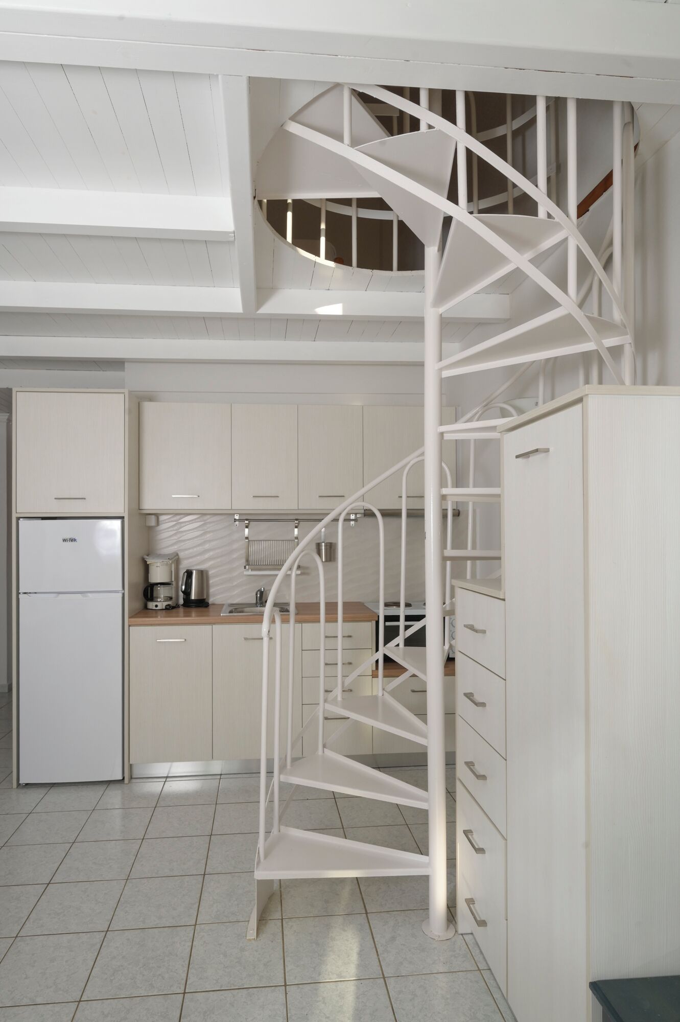 A kitchen with a white spiral staircase leading to an upper level.