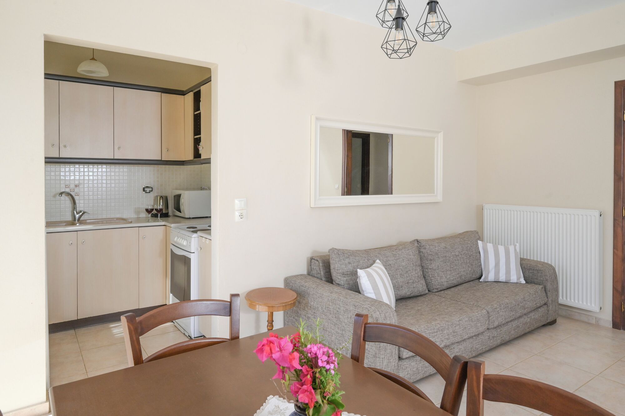A compact living space with a kitchenette, a dining table with chairs, and a sofa with cushions.