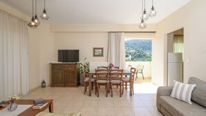 Sala de estar con sofá, mesa de comedor, sillas, televisor y vista al exterior.